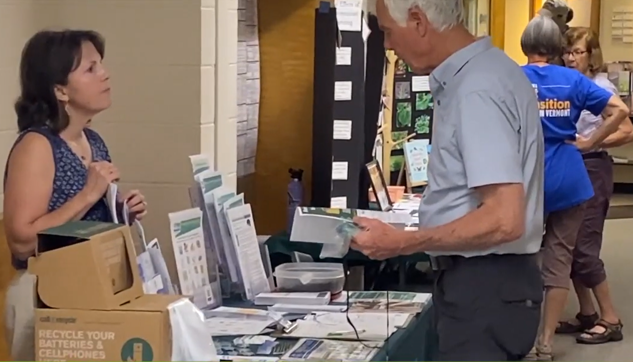 Alliance representative standing behind a display table of printed materials speaking an event attendee.