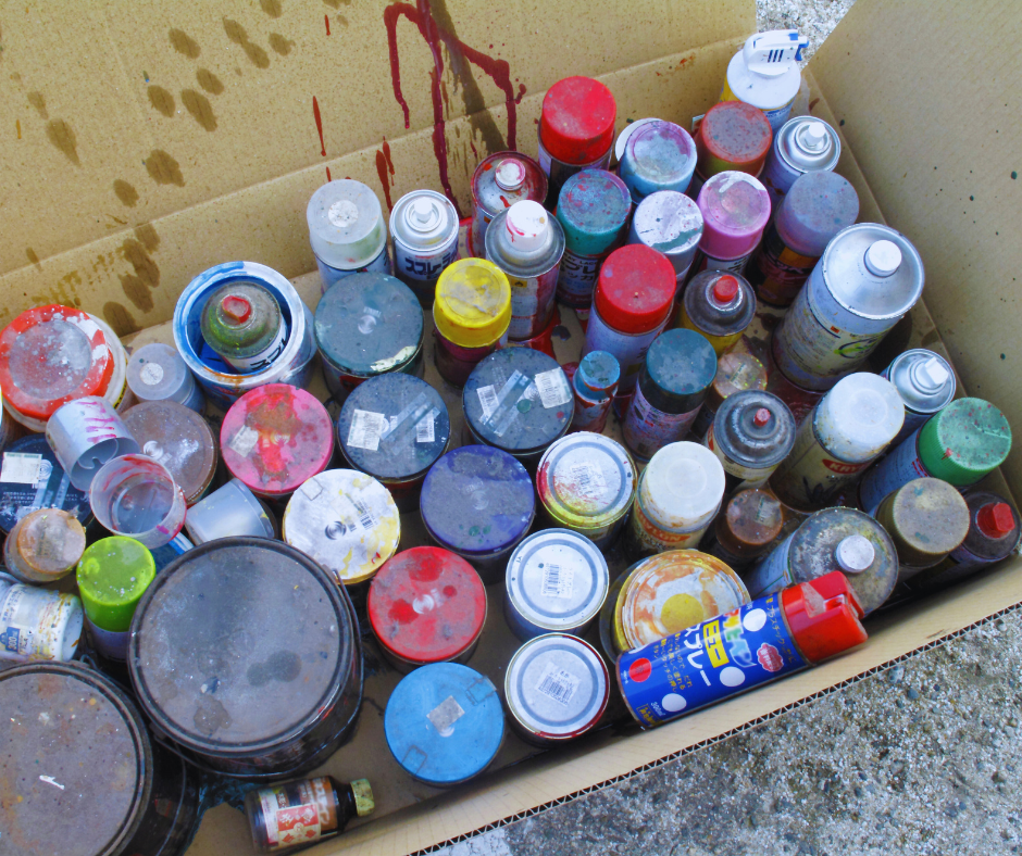 A cardboard box filled with cans of spray paint and architectural paint.